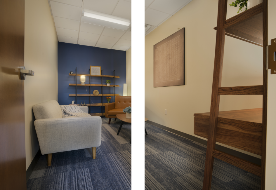 A small modern office space with a light gray sofa, a tan armchair, a blue accent wall with shelves, a round wooden table, and a wooden ladder in the foreground. The room has patterned blue carpet and beige walls.